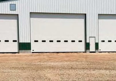 Metal garage with three overhead doors, frame opening trim, walk door, wainscot, and metal louvre.